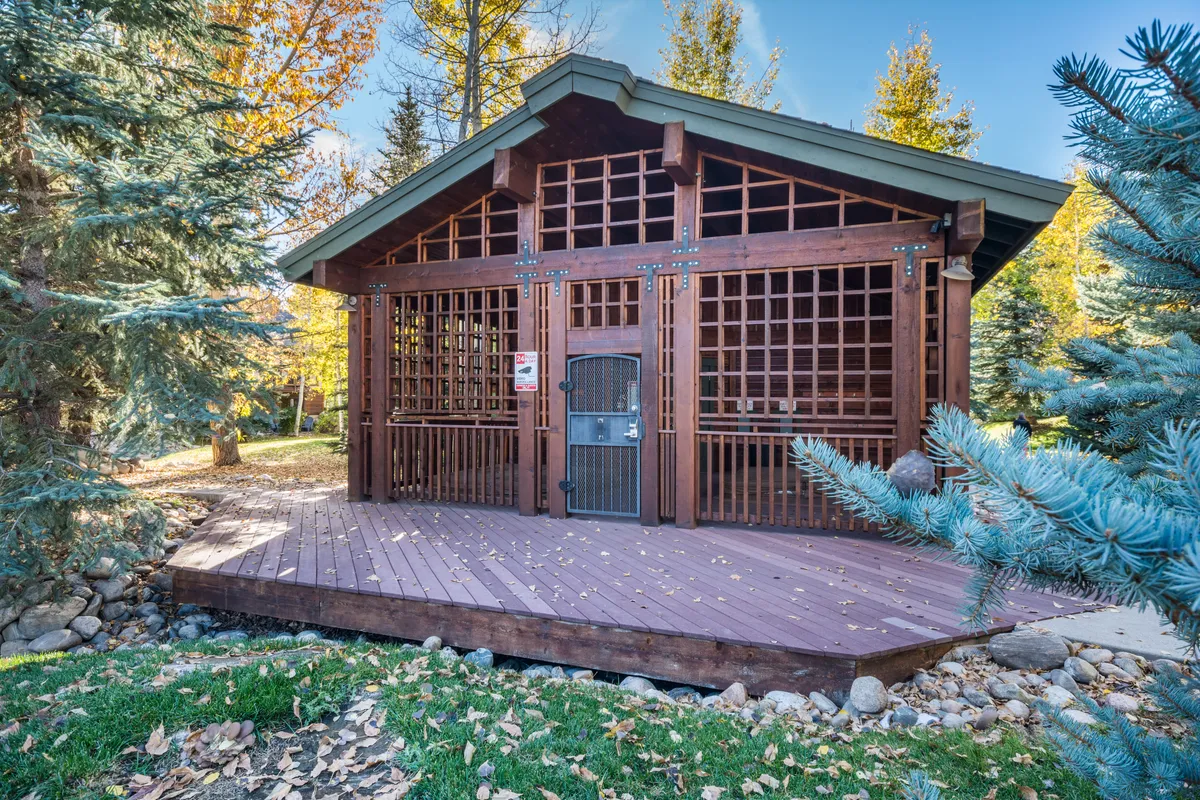 An exterior shot showcasing a wooden structure with lattice work and a spacious deck area, surrounded by greenery. The outdoor space appears tranquil and inviting, ideal for gatherings or relaxing while taking in the environment. The deck connects the home to the outdoors and the community beyond.