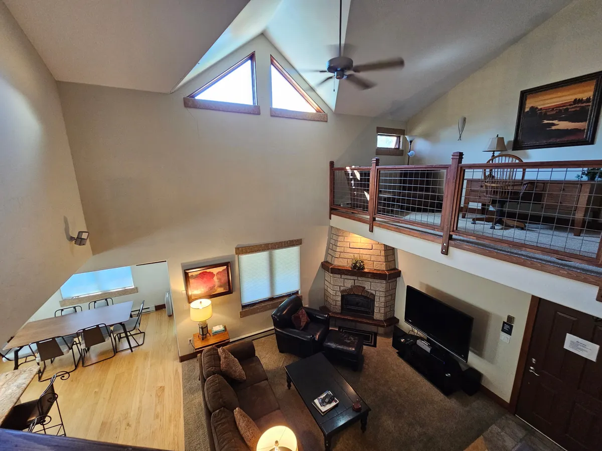 A welcoming living and dining area featuring a fireplace, a plush sofa set, a modern dining area, and expansive windows looking onto greenery. There's a sense of warmth and conviviality, with room for family gatherings, entertaining, or simply unwinding by the fire.