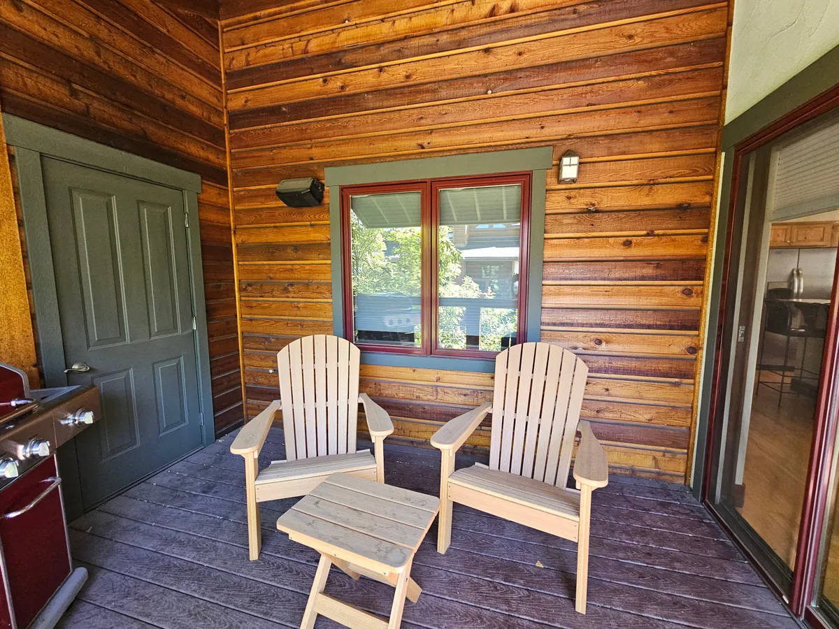 A cozy outdoor seating area with wooden chairs and a small table sits beside a glass door and wooden walls. The space is ideal for relaxing, reading, or socializing with friends after a day on the slopes, and hints at the enjoyment of sunrise views or star gazing in the evenings.