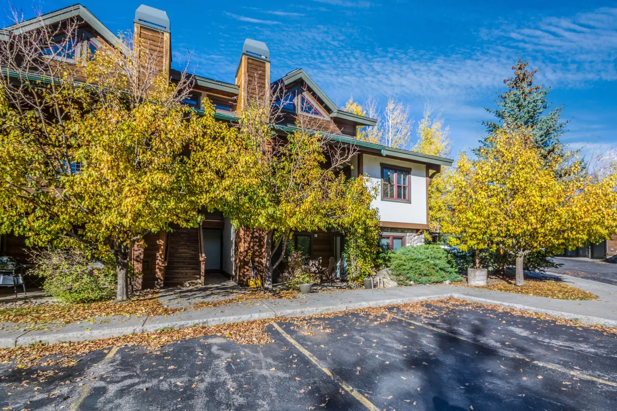 This exterior image displays the property surrounded by lush yellow autumn trees, with clear blue sky and inviting architectural details. The porch and visible communal areas suggest a welcoming, social atmosphere and proximity to the outdoors.