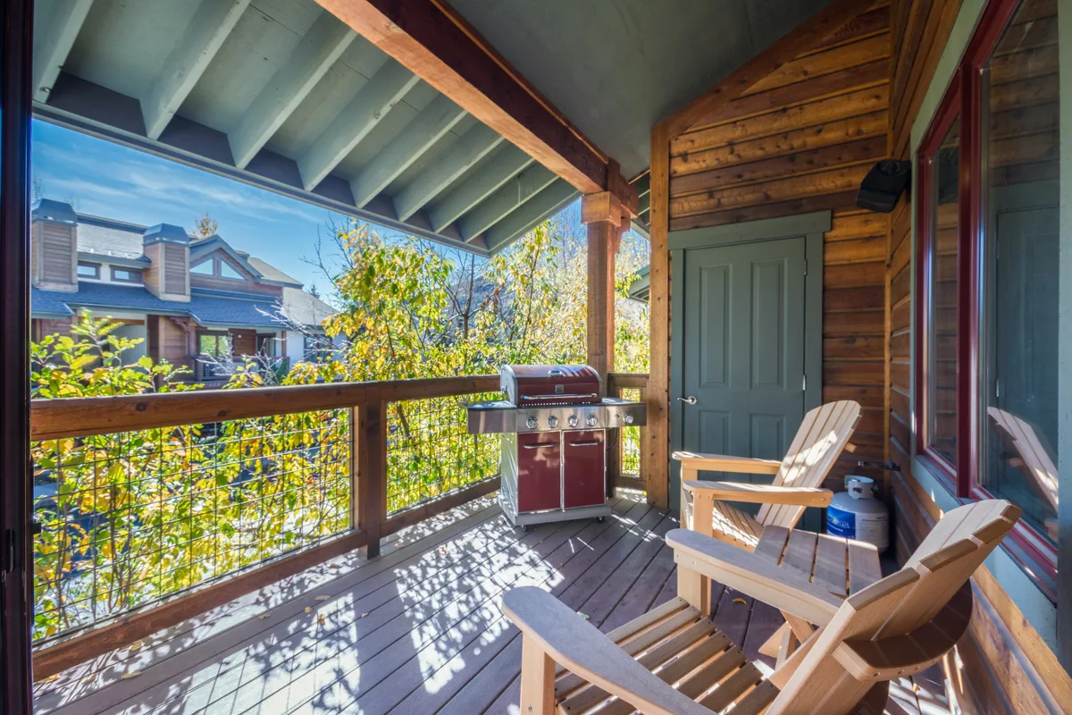 An exterior view showcasing an outdoor grill, wooden chairs, and beautiful natural scenery. The area is inviting for relaxing or socializing after a day out, with views suggesting proximity to local conveniences and outdoor enjoyment.