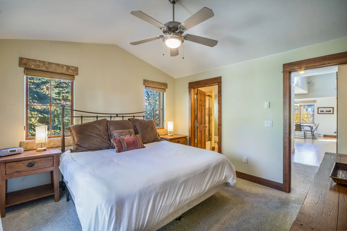 A calm and bright bedroom featuring a comfortable bed, windows with abundant natural light, nightstands, and a doorway. The space feels inviting, ideal for enjoying a quiet moment, reading, or watching the sunrise from bed.