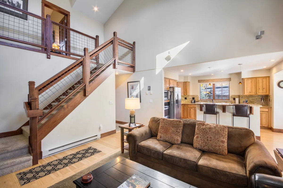A view of a warm interior showing a staircase, a comfortable sofa for lounging, a kitchen island, and a window with outside views. The area is bathed in natural light, suggesting a welcoming space for both work and relaxation.