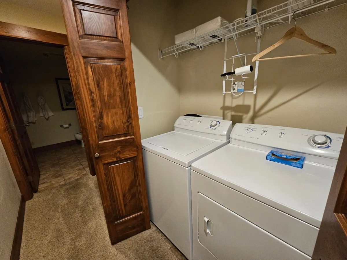This image features a modern laundry area with a washing machine, dryer, wooden door, and a shelf with hangers above. The space appears organized and functional, highlighting the practical side of in-unit amenities.