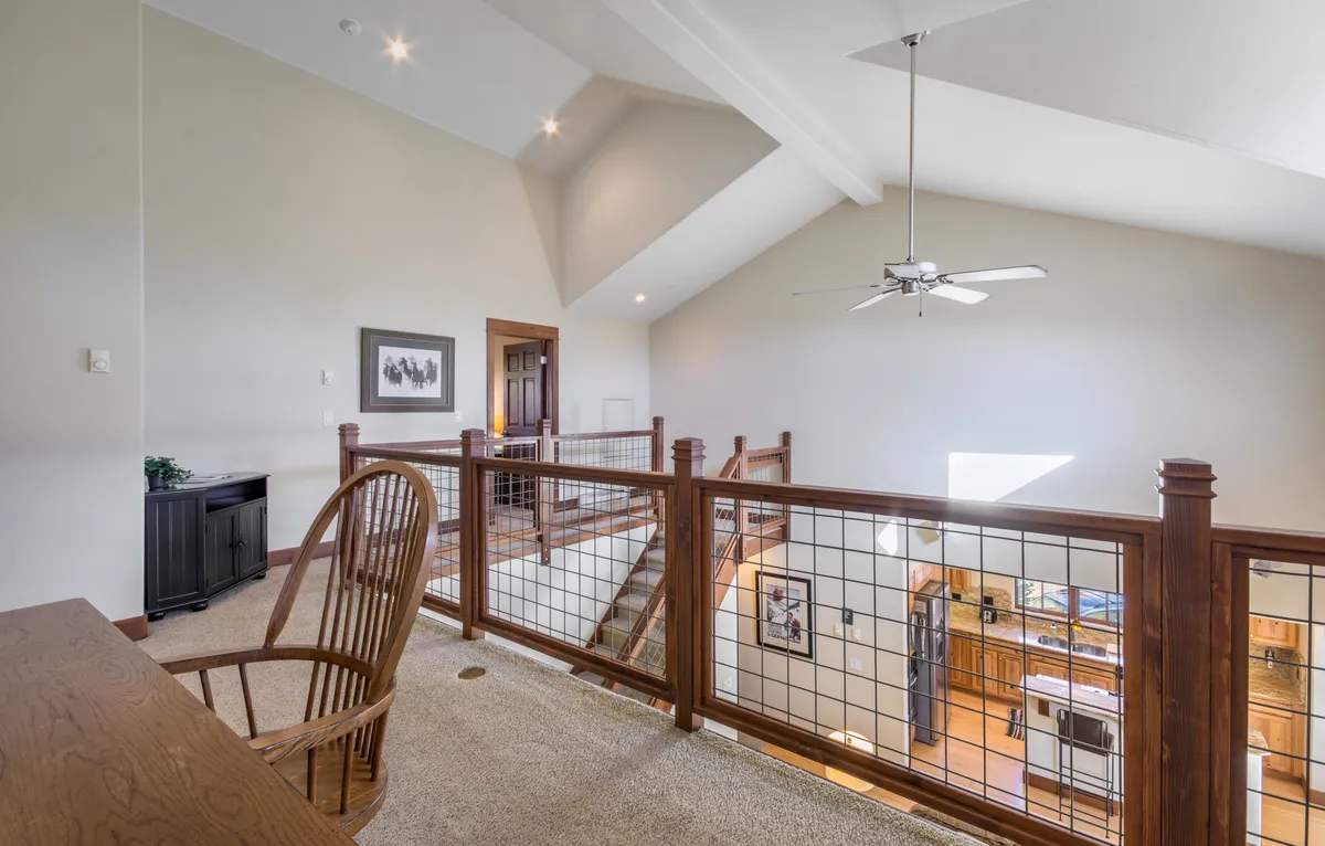 The photo shows an open loft area with a wooden railing, ceiling fan, and large windows, connected visually to the living area below via the staircase. The open layout and abundance of natural light create a sense of both connection and separation, echoing the section’s description of the loft’s dual qualities.