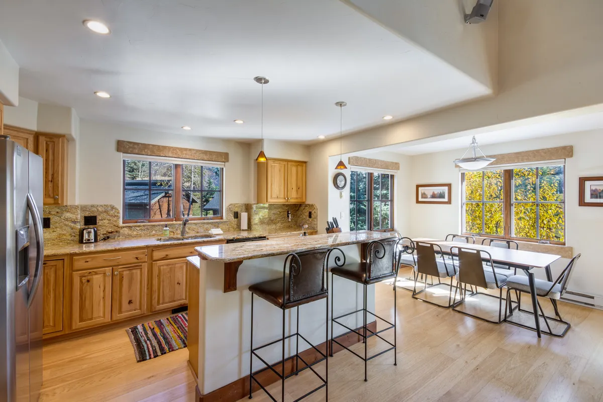 A bright, inviting kitchen and dining area with a large island, bar stools, a spacious dining table, and big windows that hint at the neighborhood outside. The space is set up for cooking, entertaining, and socializing—activities that complement a lifestyle with easy access to local shops and dining.